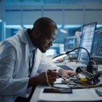 Modern Electronics Research, Development Facility: Black Male Engineer Does Computer Motherboard Soldering. Scientists Design PCB, Silicon Microchips, Semiconductors. Medium Closeup Shot