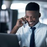 Shot of a young businessman talking on a cellphone while working on a laptop in an office at night